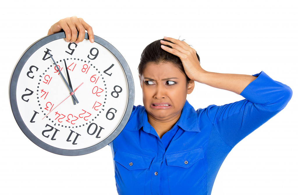 An employee holding a clock very stressed, pressured by lack of and running out of time late for a meeting