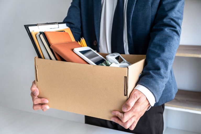 businessman carrying packing up all his personal belongings and files into a brown cardboard box has frustrated and stressed to resignation and signing cancellation contract letter.