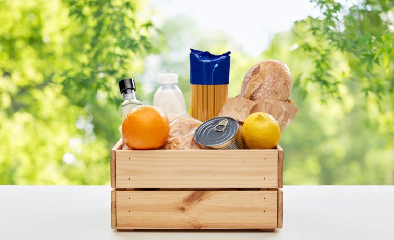 grocery and delivery concept - food in wooden box on table over green natural background